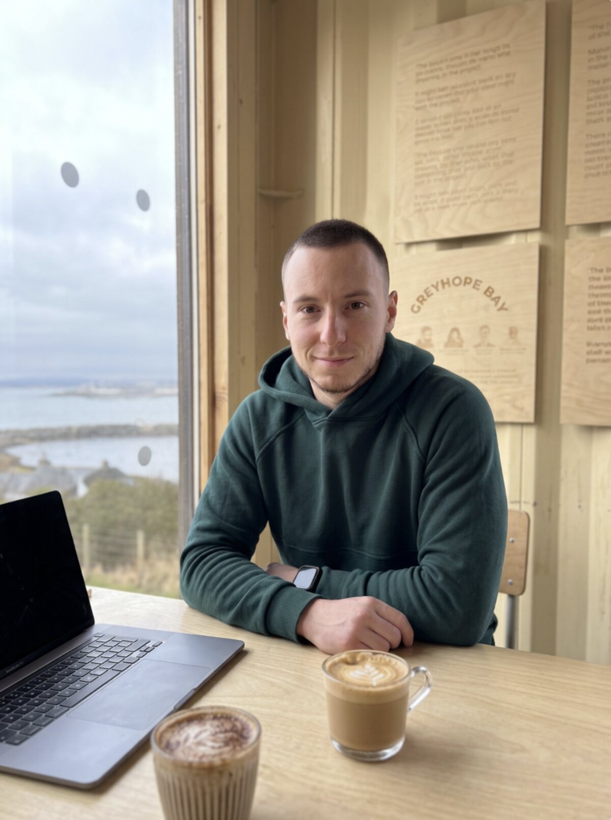 Vitalii Loboda, founder of Scotland Websites, working on a laptop in a coffee shop overlooking Aberdeen bay